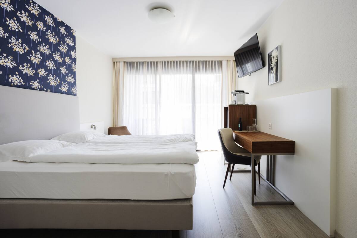 A hotel room with a bed, a desk, a chair, a television, and a window with curtains.