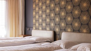 Habitación de hotel con dos camas, cabecera con diseño geométrico y ventana con cortinas.