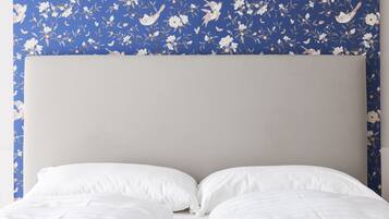 Ein Bett mit weißer Bettwäsche und einem schlichten Kopfteil vor blumigem, blauem Wandpapier.