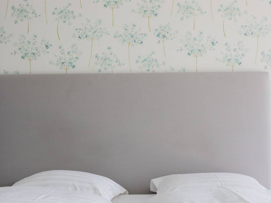 Una cama con ropa blanca y un cabecero, frente a una pared con estampado floral.
