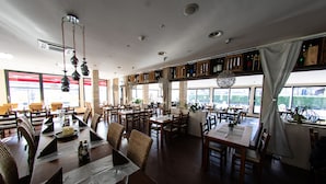 Un restaurante espacioso con varias mesas y sillas, ventanas amplias y lámparas colgantes.