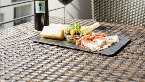 Una mesa con una botella de vino, una copa de vino y un plato de comida en un balcón con vistas a las montañas.