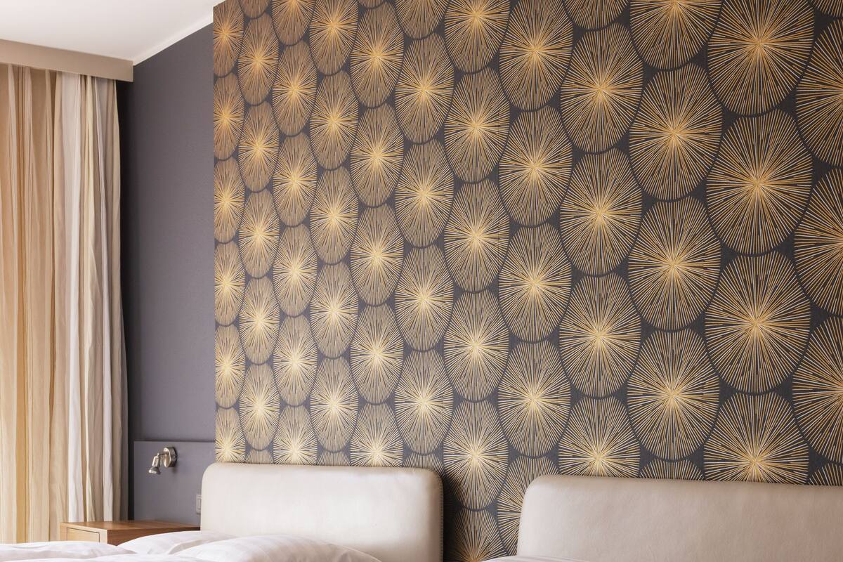 A hotel room with two beds, a dark patterned headboard, and a nightstand with a lamp.
