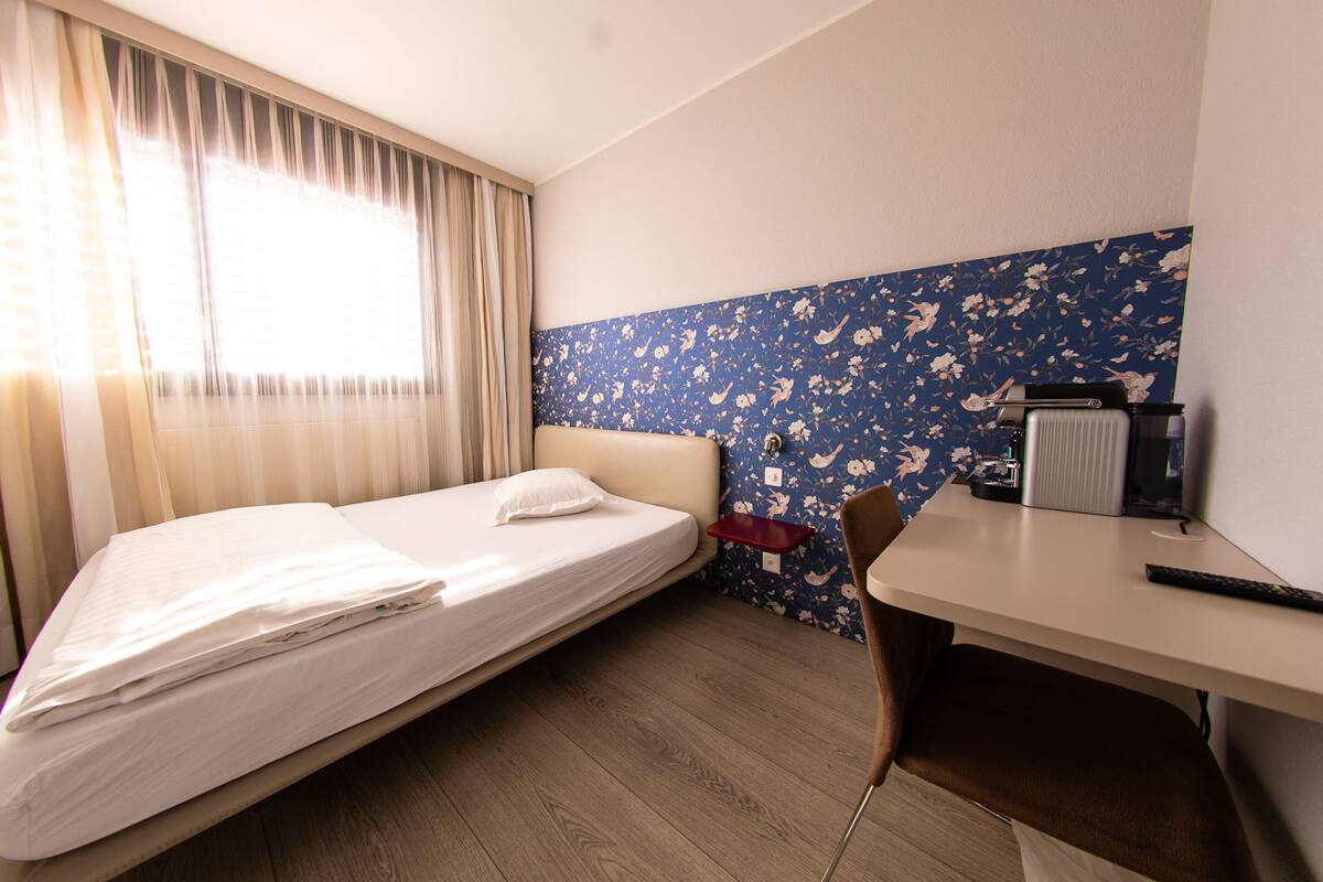 A hotel room with a bed, a desk, a chair, and a window with curtains.
