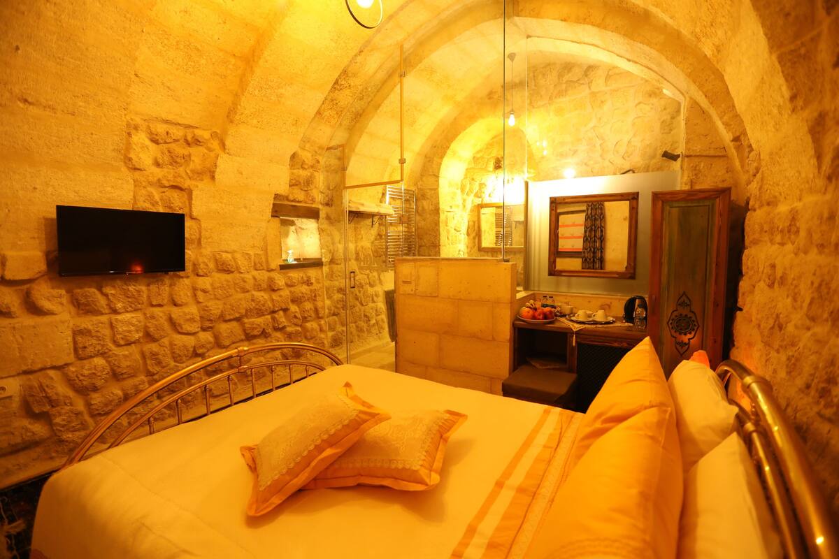 A room with a stone wall, a bed with yellow bedding, a flat-screen TV mounted on the wall, and a wooden cabinet.
