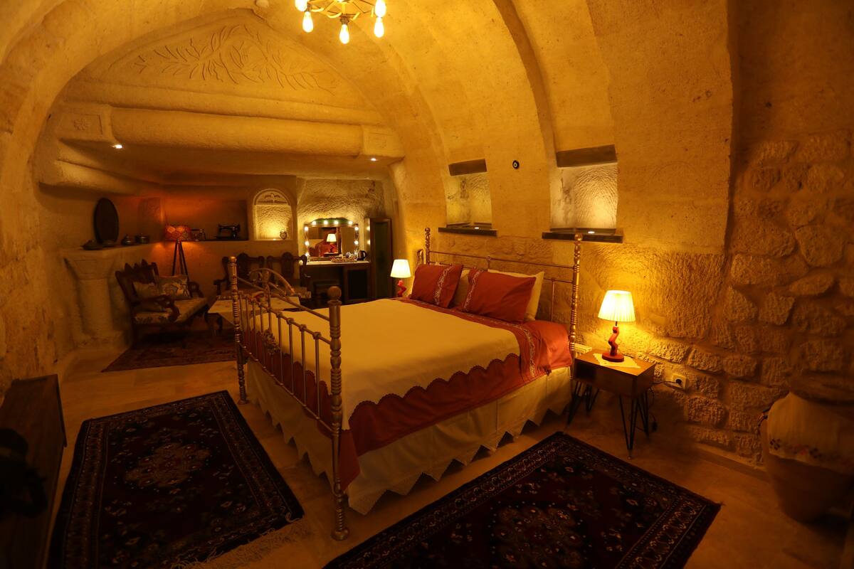 A bedroom with a four-poster bed, a stone wall, and a chandelier.