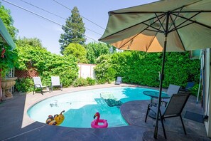 Un patio trasero con piscina, sillas de descanso y una sombrilla.