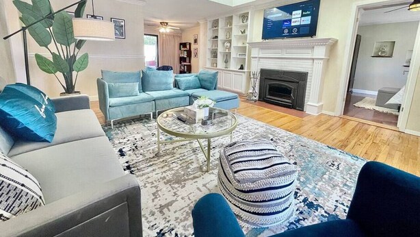 A living room with a sofa, armchair, ottoman, coffee table, fireplace, TV, and a plant. - Family Retreat • Pool • Air Hockey • King Suite (Chico)