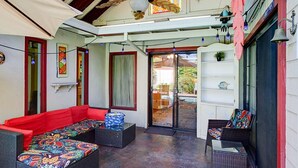 A covered patio with wicker furniture, a red sofa, and a glass door leading outside. - Family Retreat • Pool • Air Hockey • King Suite (Chico)