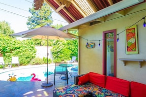 Um alpendre coberto com piscina, mesa e um sofá colorido.