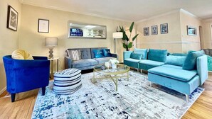 A modern living room with a blue sofa, a blue armchair, a coffee table, and a patterned rug. - Family Retreat • Pool • Air Hockey • King Suite (Chico)
