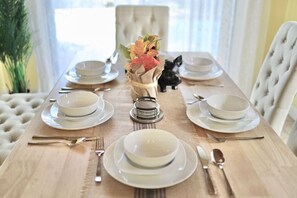 Mesa de comedor preparada para cuatro personas, con platos blancos, cubiertos y un centro de mesa con hojas otoñales.