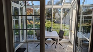 A conservatory with a table and chairs, a view of a garden, and a stone pathway.