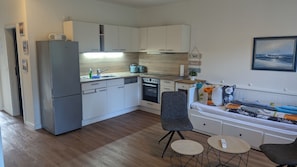 Una cocina compacta con muebles blancos, horno empotrado y un rincón comedor con sofá y dos sillas.