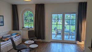 A room with a bed, a desk, a chair, a small table, and a large sliding glass door leading to an outdoor patio.