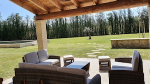 An outdoor patio with wicker furniture and a stone bench, overlooking a grassy area with trees. - Spacious and quiet farmhouse in Isle sur la Sorgue (L'Isle-sur-la-Sorgue)