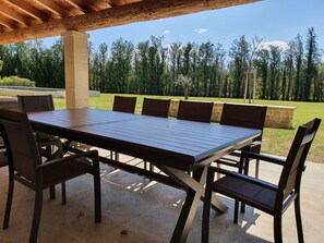 Una terrazza esterna con un tavolo e sedie di legno, circondata da un muro in pietra e affaccio su una zona boschiva.