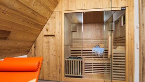 Een sauna met houten wanden en een glazen deur, met een bankje en een klein tafeltje met een handdoek.