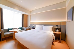 A hotel room with a large bed, a bedside table, a small round table with a chair, a sofa, and a large window. - Ji Hotel (Chengdu)