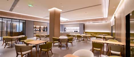 A modern dining area with tables and chairs, a kitchen in the background, and a clean, well-lit interior.