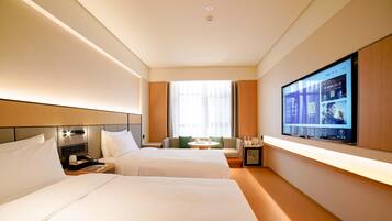 A hotel room with two beds, a TV, a small table, and a seating area.