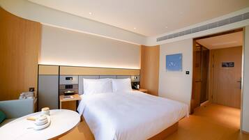 A modern hotel room with a large bed, bedside tables, a small round table with a teapot, and a wooden headboard.