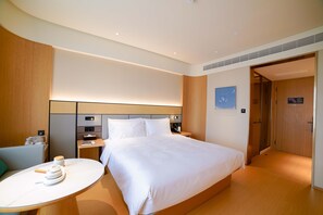 A modern hotel room with a large bed, bedside tables, a small round table with a teapot, and a wooden headboard. - Ji Hotel (Chengdu)