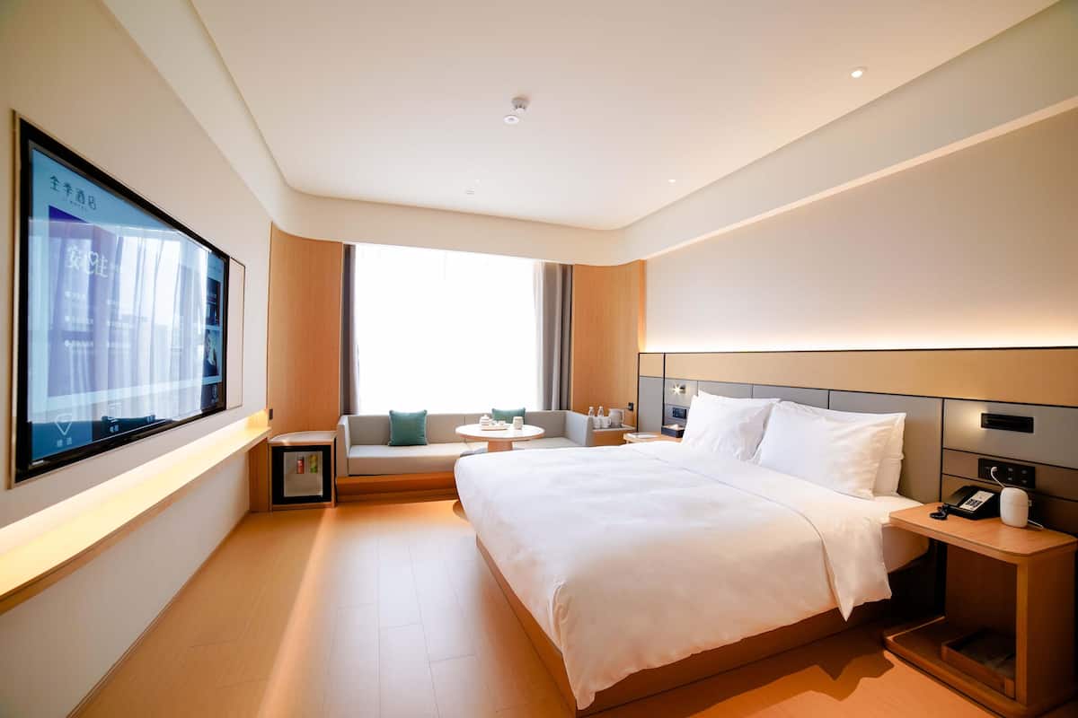 A modern hotel room with a large bed, a sofa, a small table, and a TV mounted on the wall.