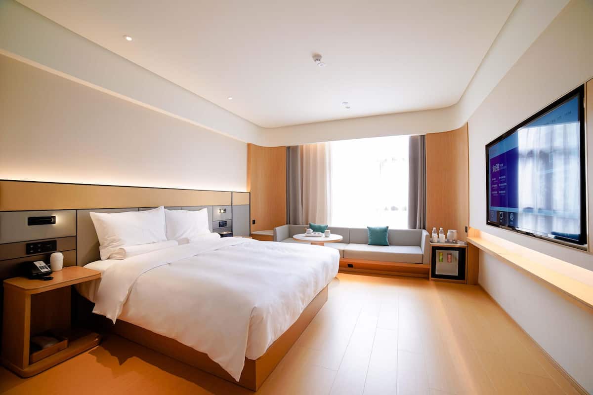 A modern hotel room with a large bed, a bedside table with a phone, a small seating area with a table, and a TV mounted on the wall.