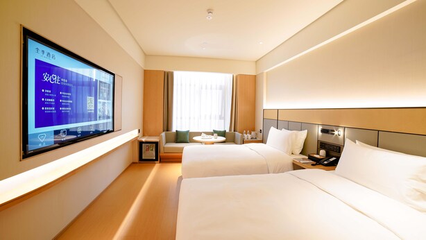 Habitación de hotel con dos camas, un televisor montado en la pared, una mesita pequeña y un sofá.