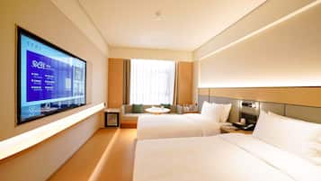 Quarto de hotel com duas camas, televisão fixada na parede, uma mesinha e um sofá.