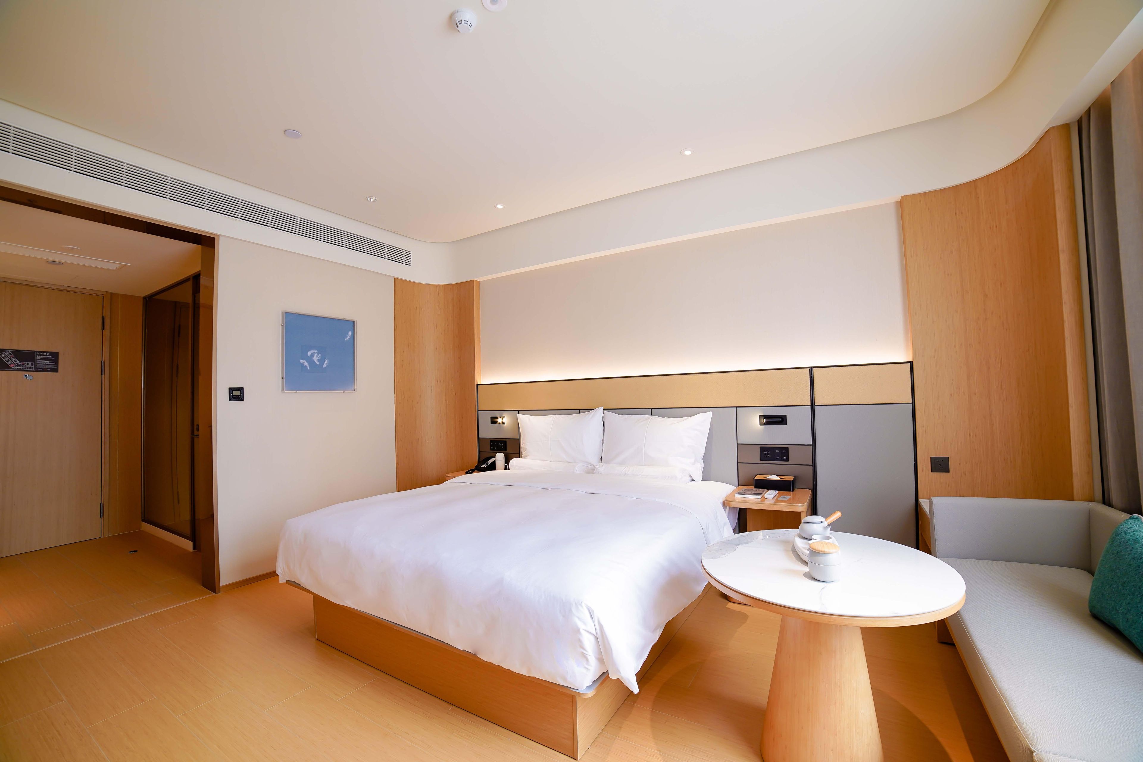 A hotel room with a large bed, bedside tables, a seating area, and a view of the outside.