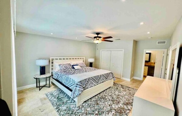 Une chambre à coucher avec un lit, des tables de chevet, un ventilateur de plafond et un tapis à motifs.