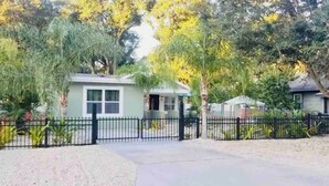 A residential property with a gated driveway, a small house, and a fenced yard with various plants. - Cozy vacation home 5 mins from downtown!!! (Sarasota)