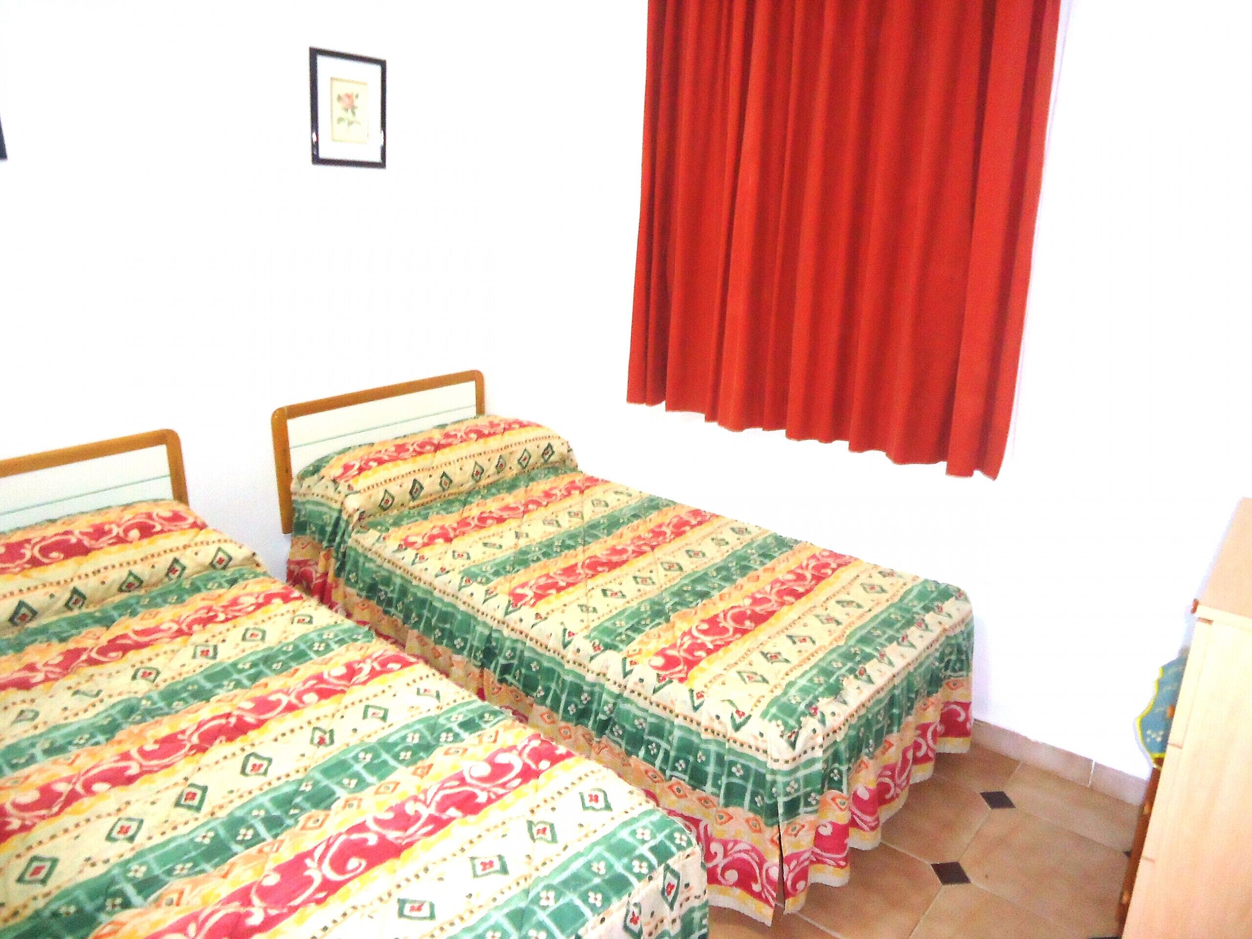 Een kamer met twee enkele bedden, een rood gordijn en een ingelijst beeld aan de muur.