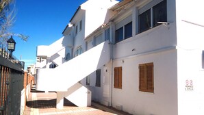 A white building with a staircase leading to the entrance, a brick-paved ground, and a black fence with a gate.