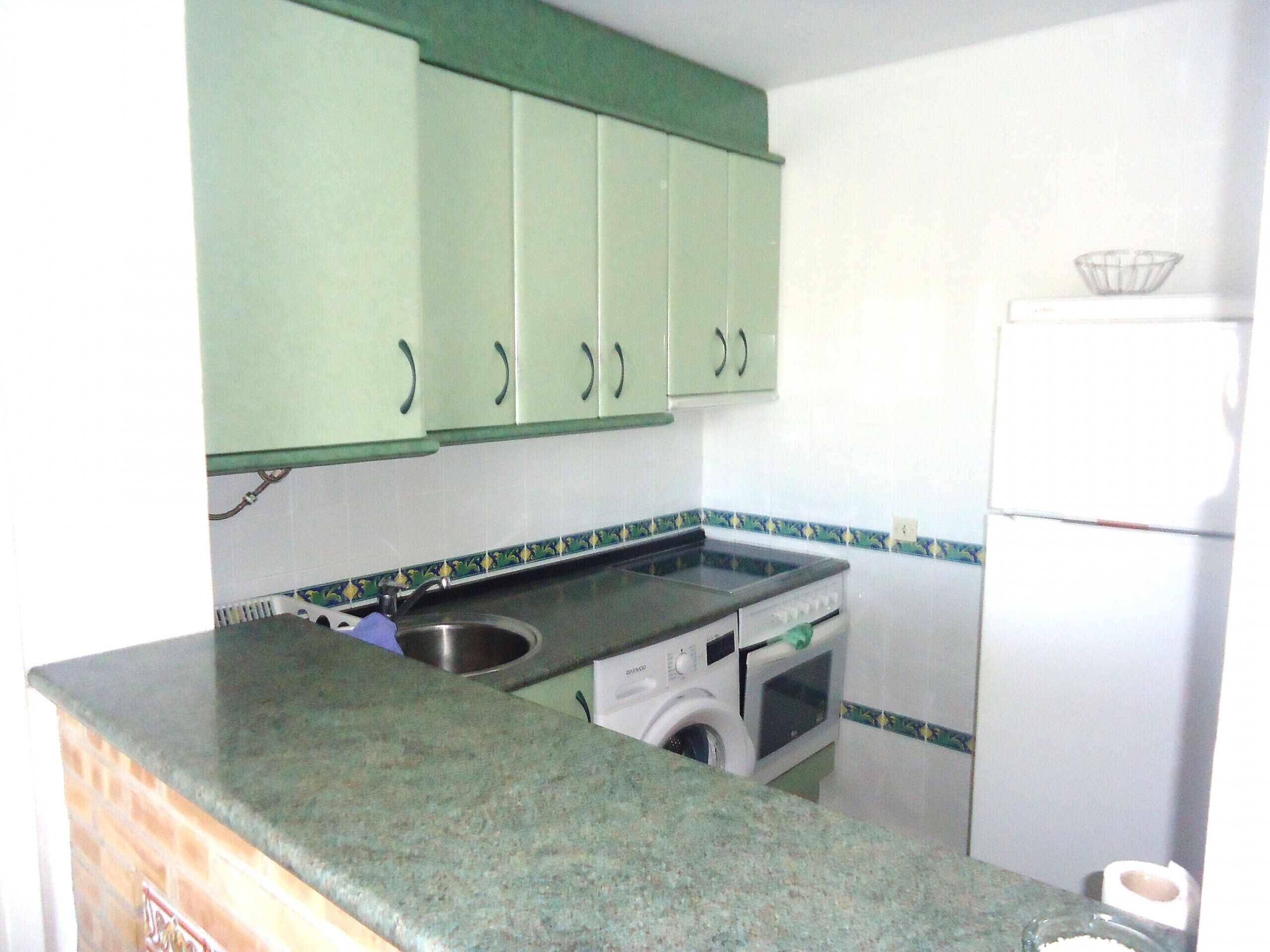 A kitchen with green cabinets, a washing machine, and a refrigerator.