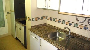 Una cocina compacta con armarios blancos, encimera de granito y pileta de acero inoxidable.