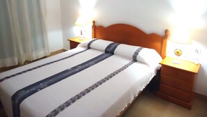 Una cama bien hecha con un edredón a rayas, dos mesitas de noche con lámparas y un cabecero de madera.