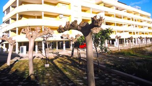 Un edificio de varios pisos con fachada curva, balcones y un estacionamiento con un coche rojo.