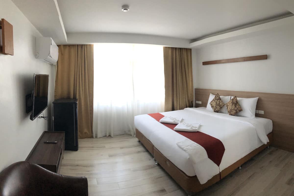 A hotel room with a bed, a TV, a desk, and a window with curtains.