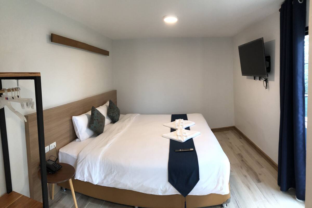 A neatly made bed with a white and navy blanket, a bedside table with a phone, and a wall-mounted TV.