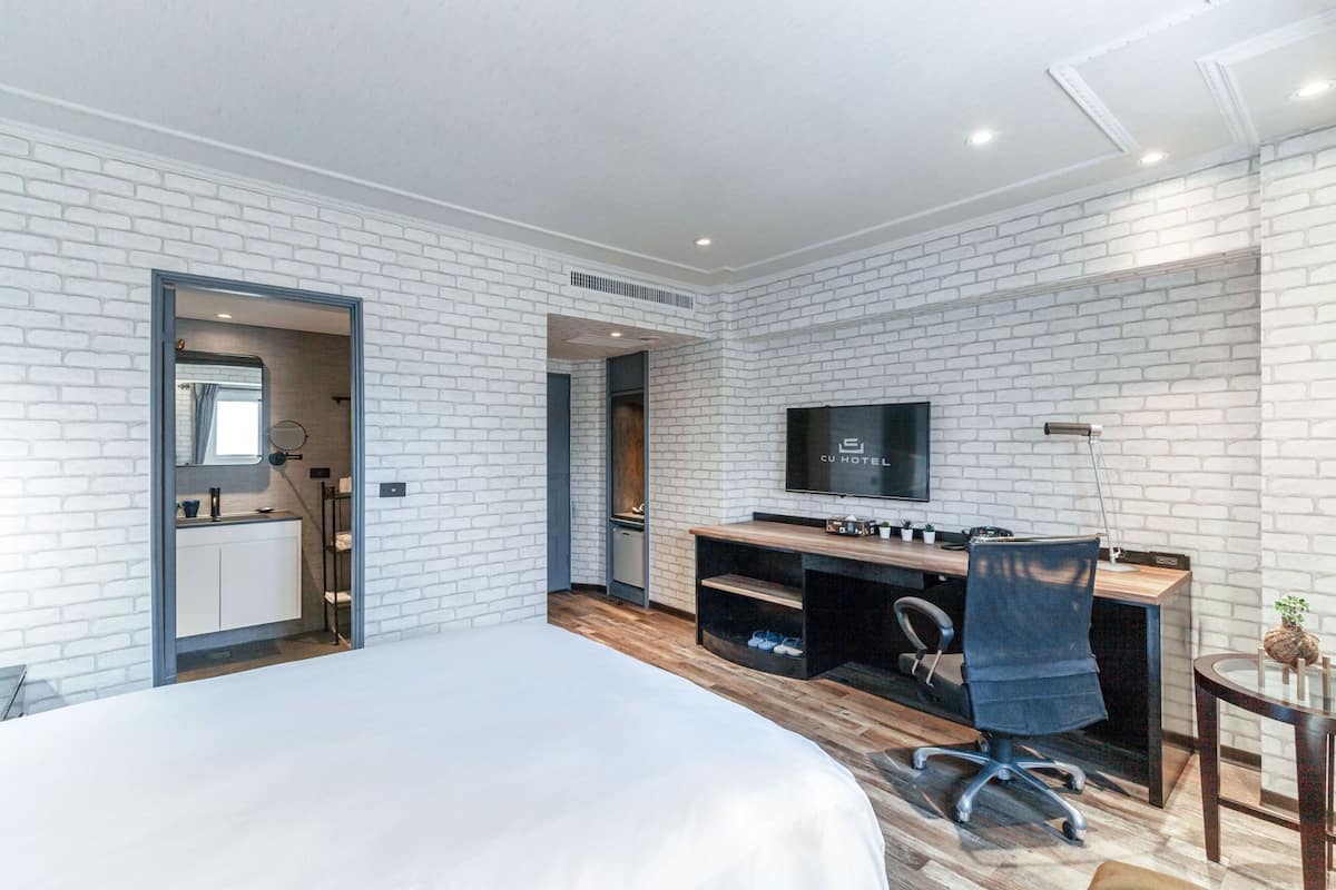 A modern hotel room with a large bed, a desk with a computer, a TV, and a small side table.