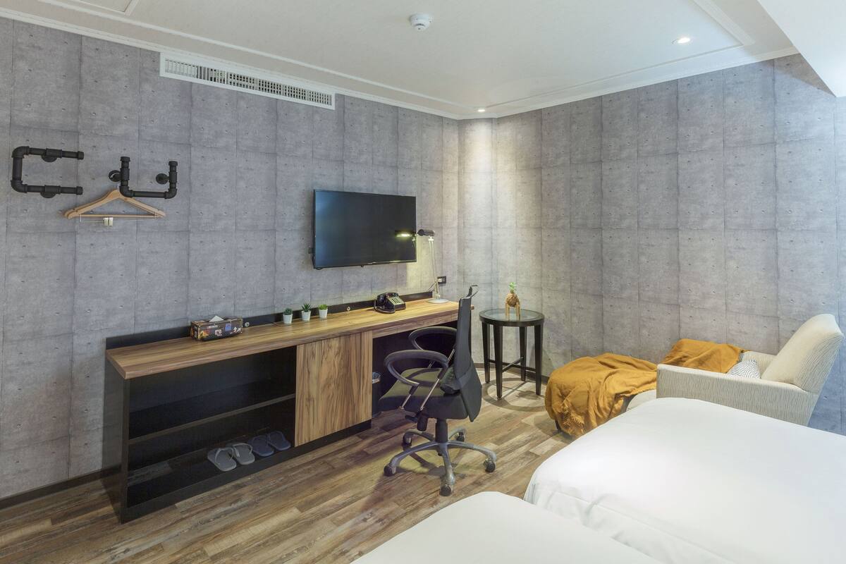 A modern hotel room with a wooden desk, a flat-screen TV, a small round table, a chair, and a bed.