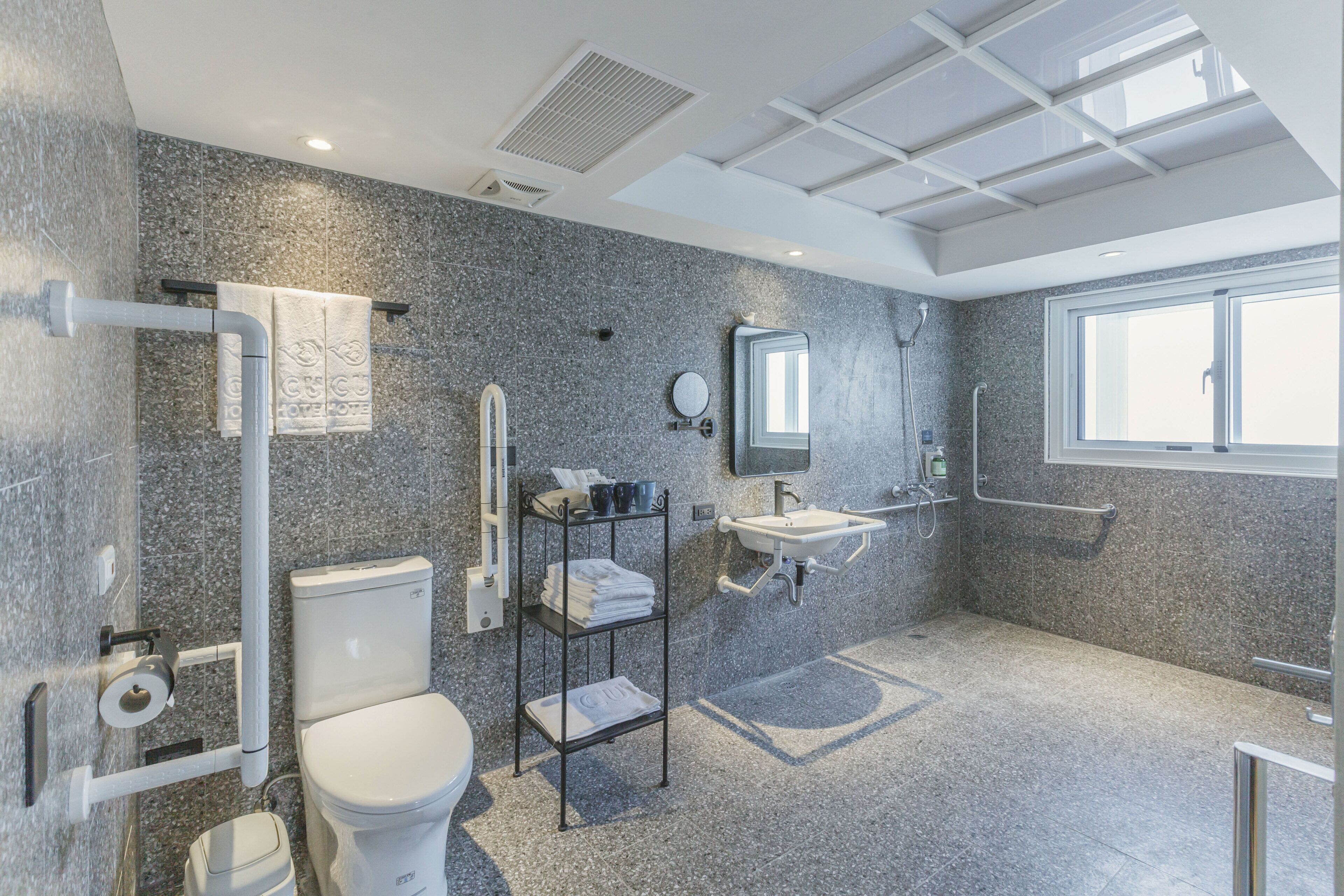 Ein modernes Badezimmer mit einer Granitwand, einer Toilette, einem Waschbecken, einem Spiegel und einem Fenster.