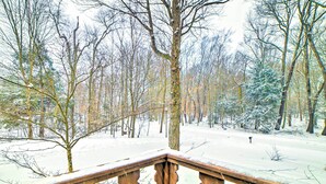 Eine Holzterrasse mit verschneiten Geländern mit Blick auf einen verschneiten Wald.
