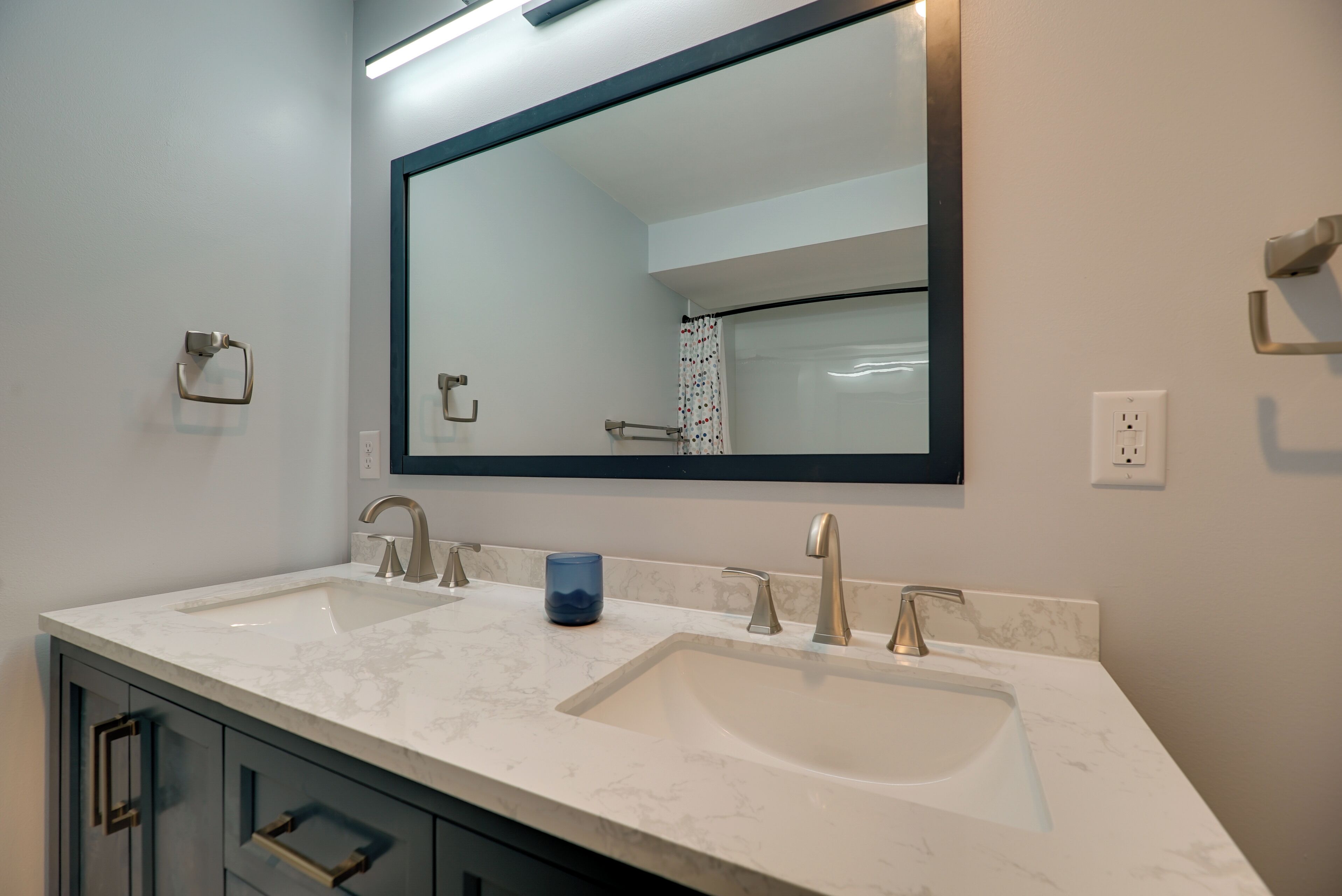 A modern bathroom with two sinks, a large mirror, and a blue cup on the counter.