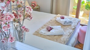 Een net opgemaakt bed met een witte deken en een roze handdoek, een vaas met roze bloemen en een klein rond tafeltje met een roze bloemstuk.