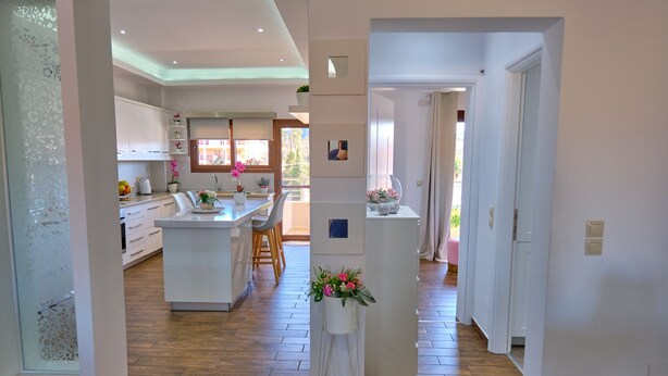Een moderne keuken met witte kasten, een centraal eiland en een eetgedeelte met stoelen.