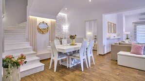 Een ruime woonkamer met een witte eettafel, witte stoelen, een beige bank en een trap.